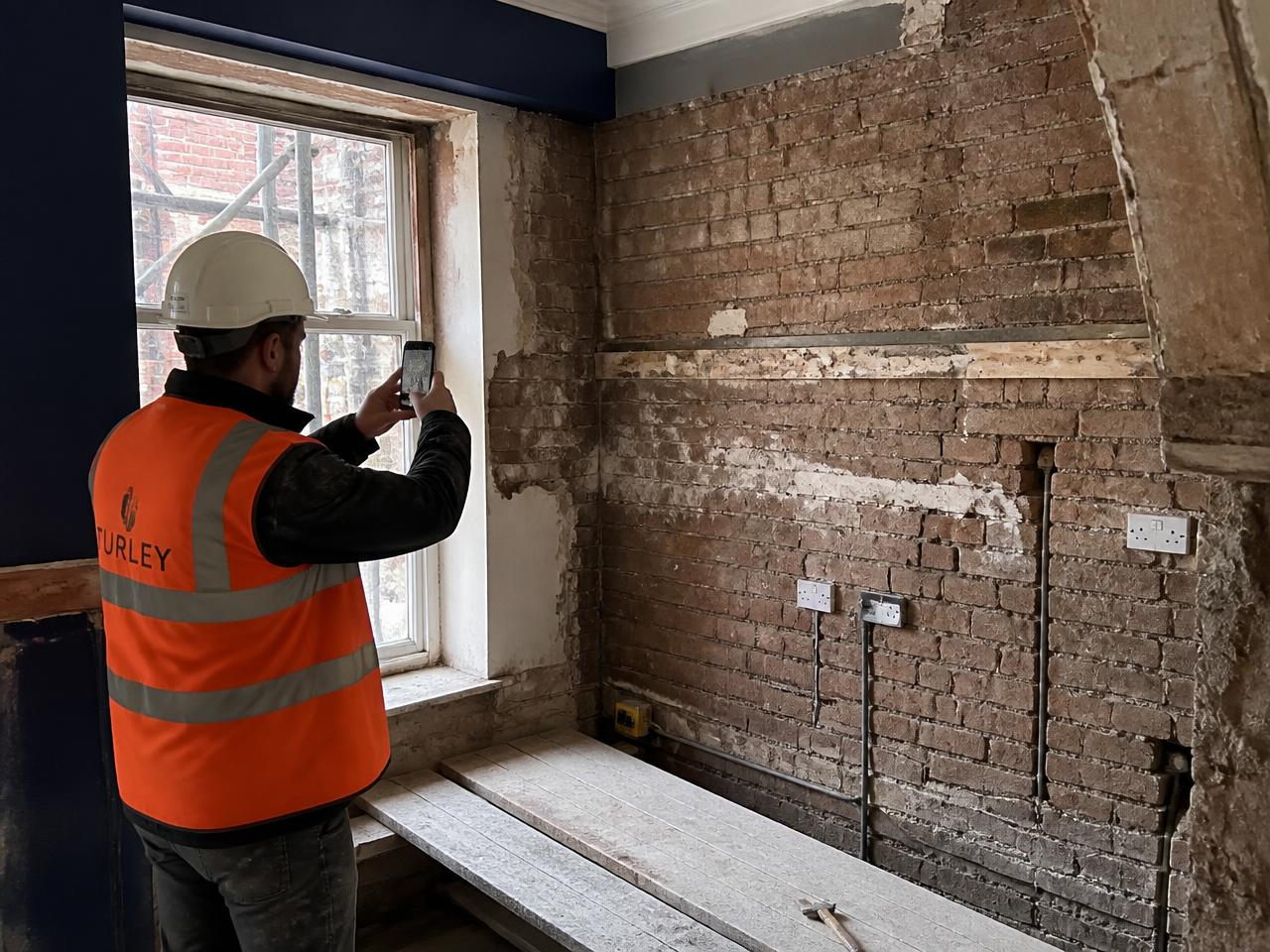 Site supervisor photographing a stripped-back kitchen wall on a UK refurbishment project